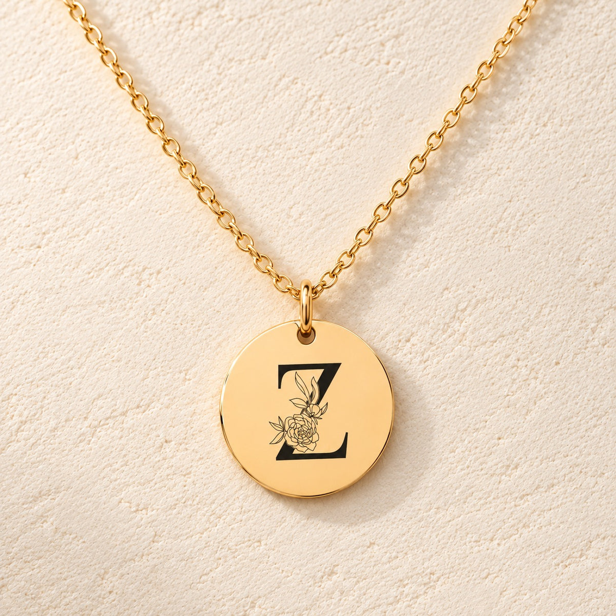 Collier initiale florale Z personnalisé doré, médaille ronde gravée avec initiale Z et fleurs, sur fond ivoire.