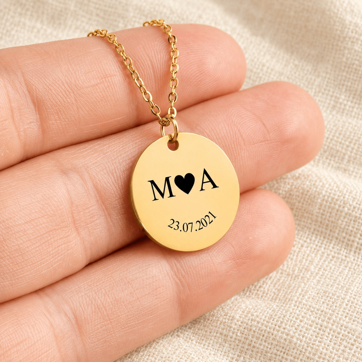 Collier initiales entrelacées Etched in Time personnalisé doré tenu en main, détail de la gravure.