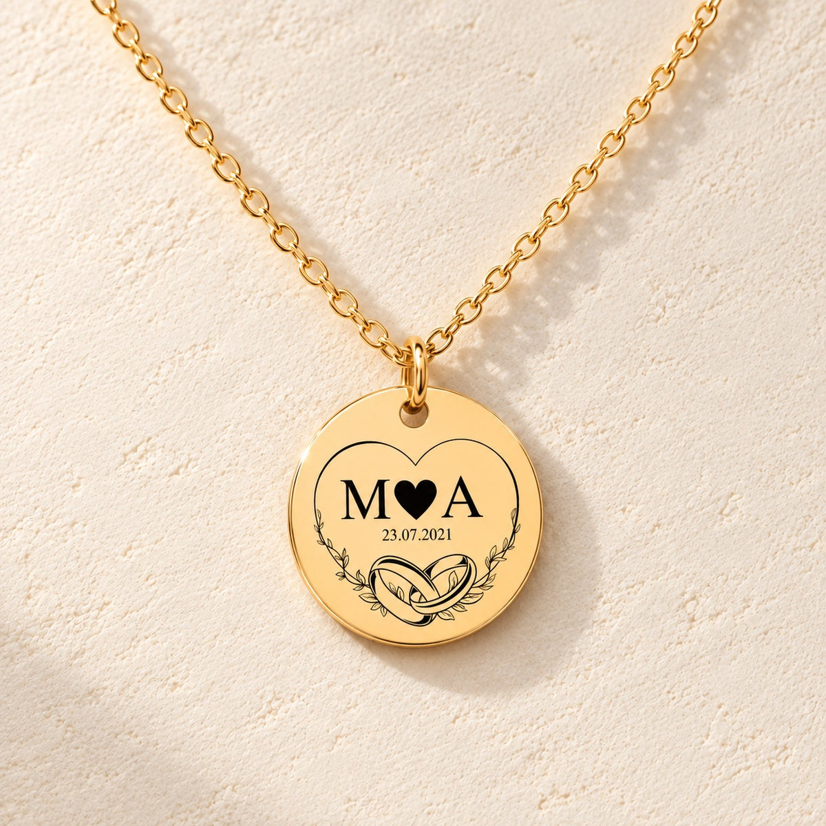 Détail de la médaille ronde dorée avec initiales M et A, deux alliances et date 23.07.2021.