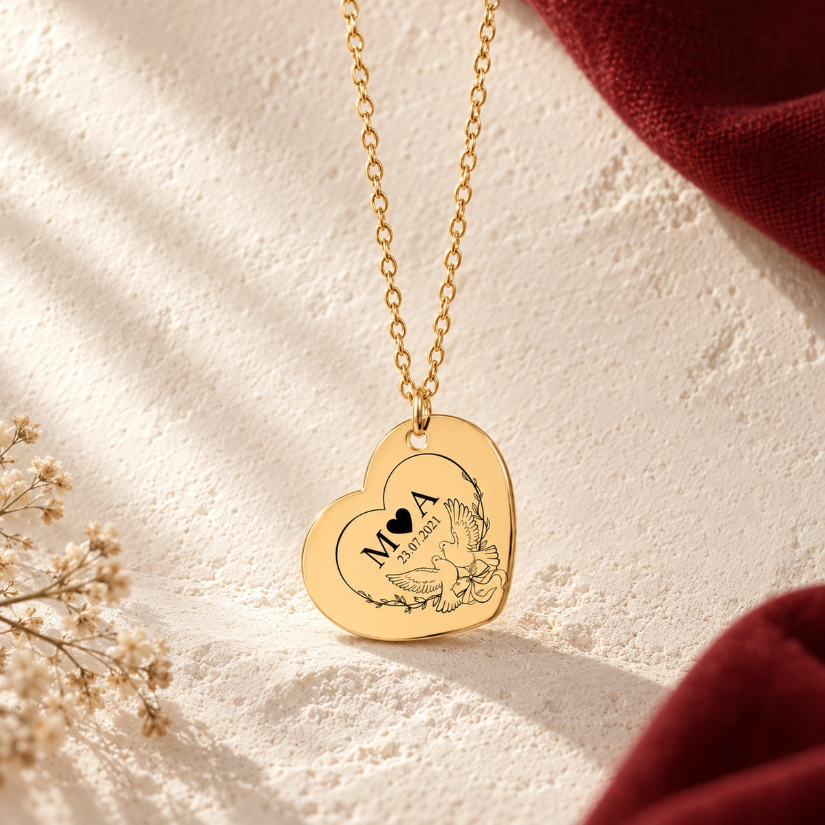 Détail du pendentif doré en forme de cœur, gravé avec deux colombes, initiales M et A et date 23.07.2021.