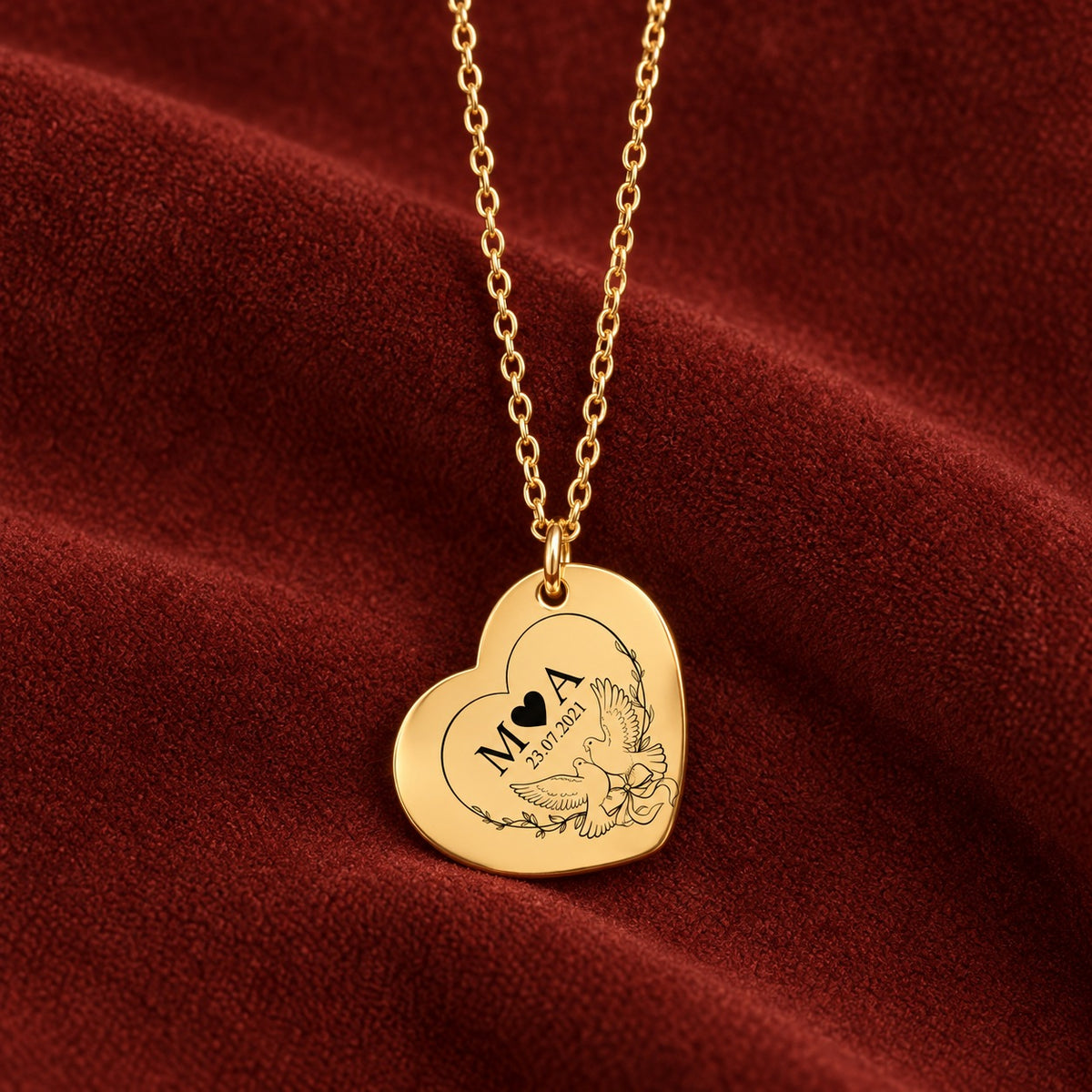 Pendentif doré en forme de cœur, gravé avec deux colombes, initiales M et A et date 23.07.2021 sur suédine rouge sanguine.