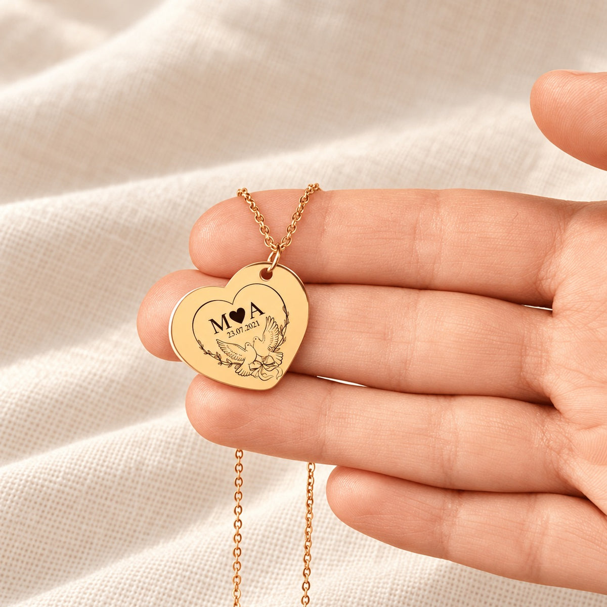 Collier Eternal Love doré tenu en main, détail du pendentif gravé.