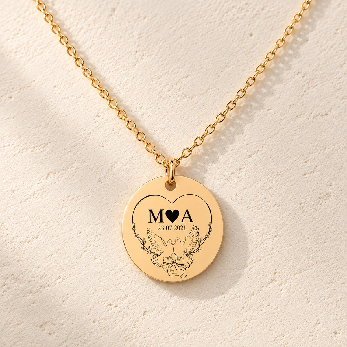 Détail de la médaille ronde dorée avec initiales M et A, deux colombes et date 23.07.2021.