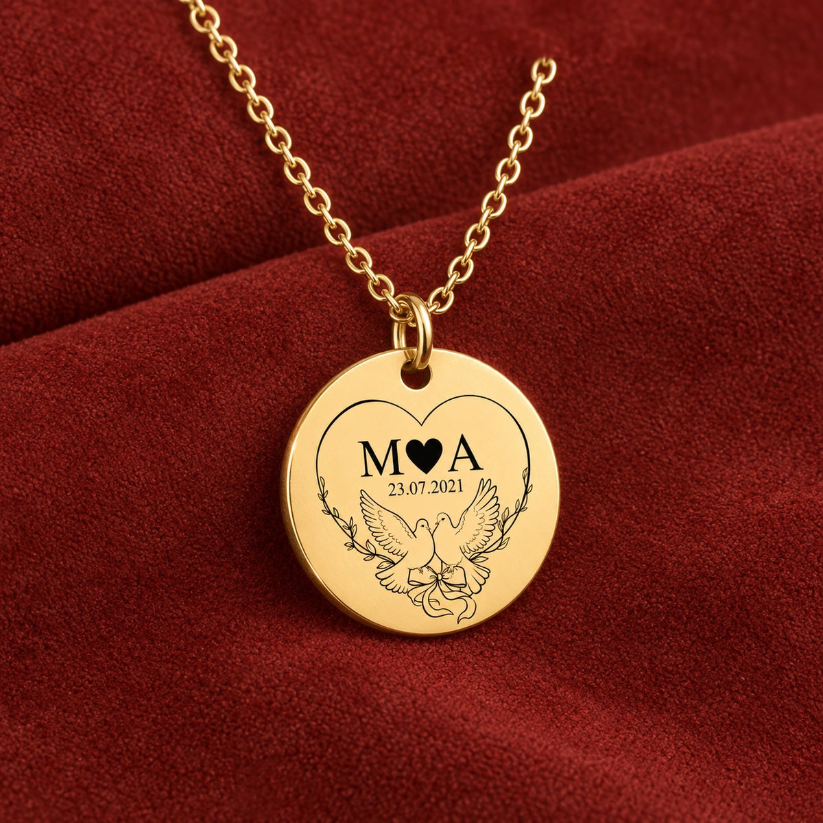 Médaille ronde dorée avec initiales M et A, deux colombes et date 23.07.2021, sur suédine rouge sanguine.