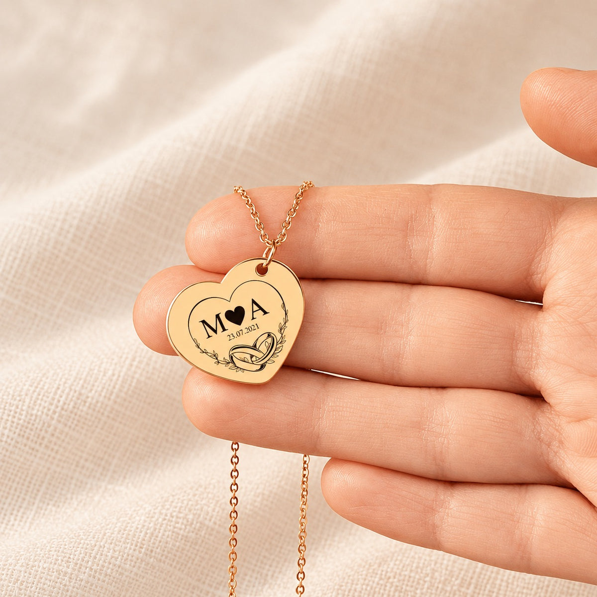 Collier Timeless Bond cœur doré tenu en main, détail du pendentif et de sa gravure.