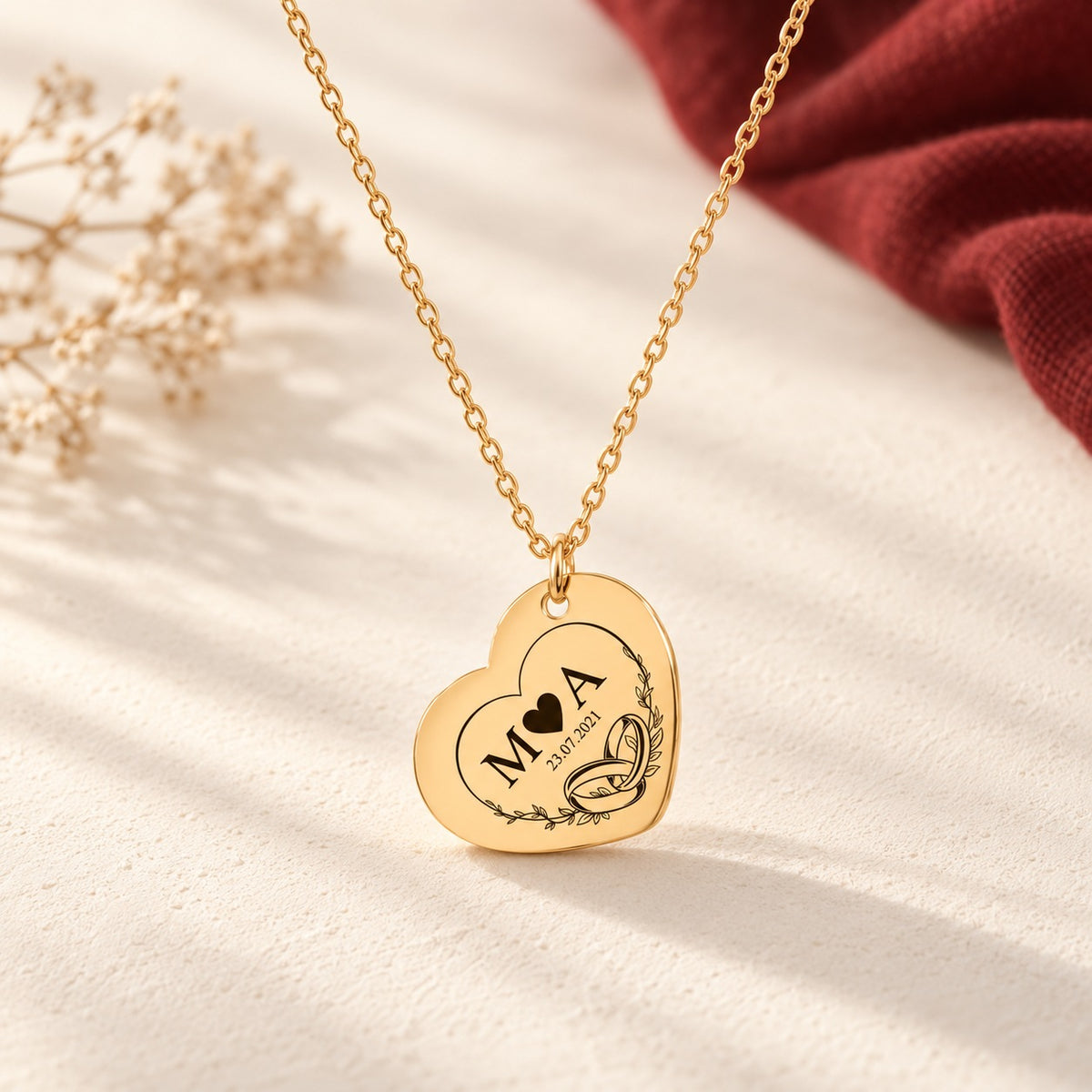 Collier Timeless Bond cœur doré avec initiales M et A, date et alliances entrelacées, sur fond ivoire.
