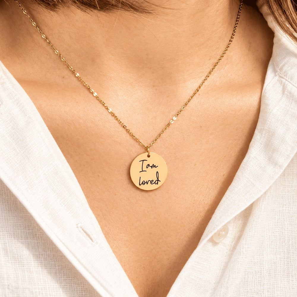 Collier Médaille Affirmations doré porté au cou, avec médaillon rond gravé.