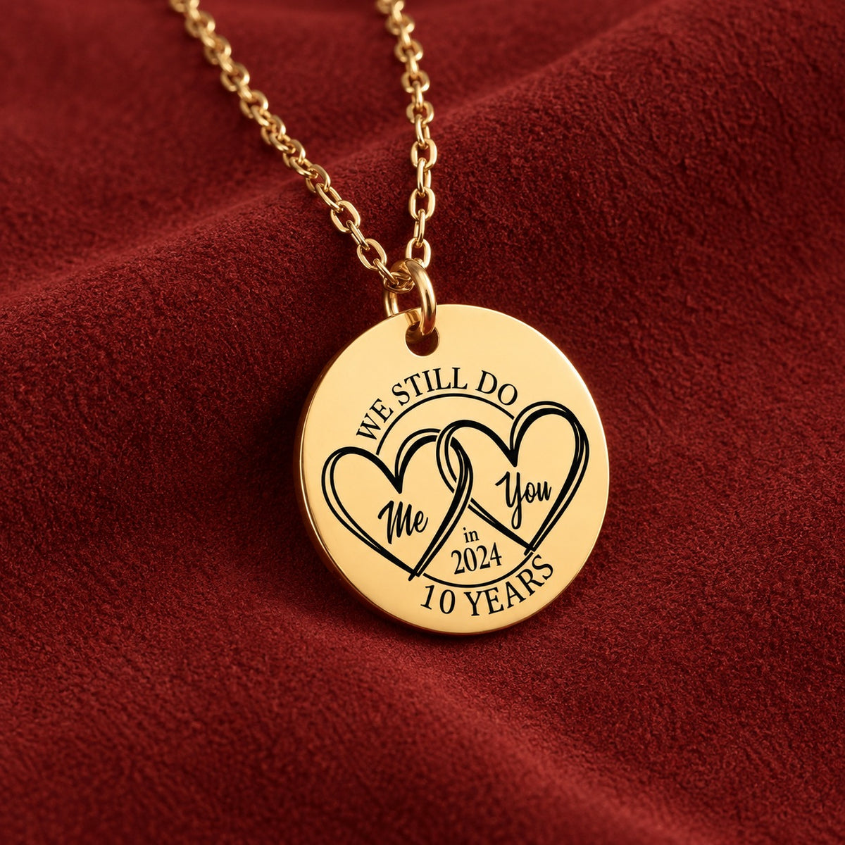 Collier médaille anniversaire de mariage 10 ans doré avec deux cœurs entrelacés et inscription « 10 YEARS », sur suédine rouge sanguine.