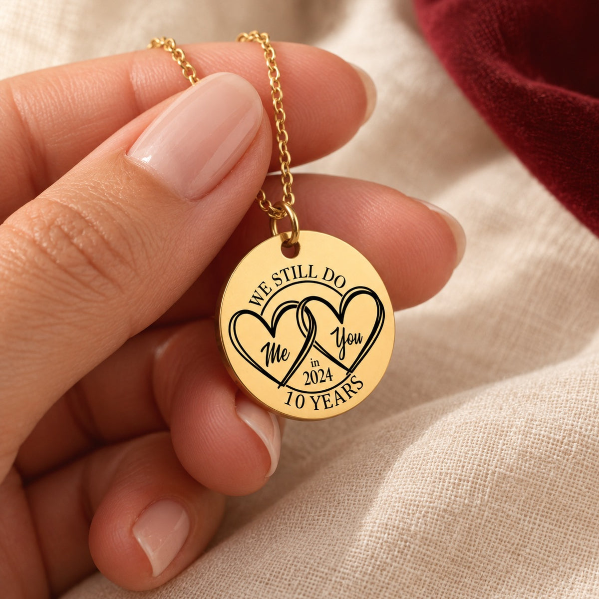 Collier médaille anniversaire de mariage 10 ans doré tenu en main, détail du pendentif et de sa gravure.