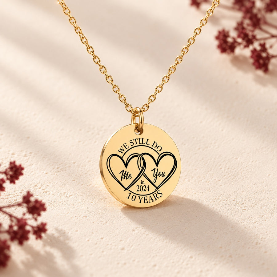 Collier médaille anniversaire de mariage 10 ans doré avec deux cœurs entrelacés et inscription « 10 YEARS », sur fond ivoire.