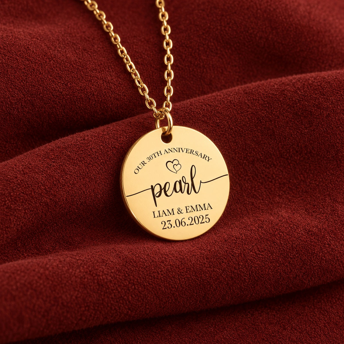 Médaille ronde dorée gravée avec inscription « pearl », prénoms Liam et Emma et date 23.06.2025, sur suédine rouge sanguine.