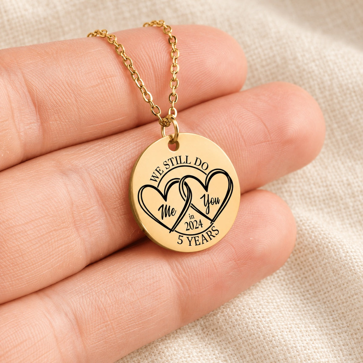 Collier Médaille Anniversaire de Mariage 5 ans doré tenu en main, détail de la gravure.