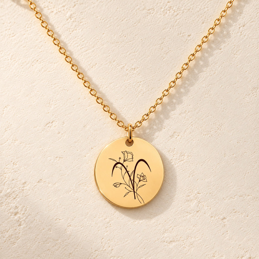 Collier médaille florale signe astrologique Bélier doré, médaille ronde gravée avec symbole du signe Bélier et fleurs, sur fond ivoire.