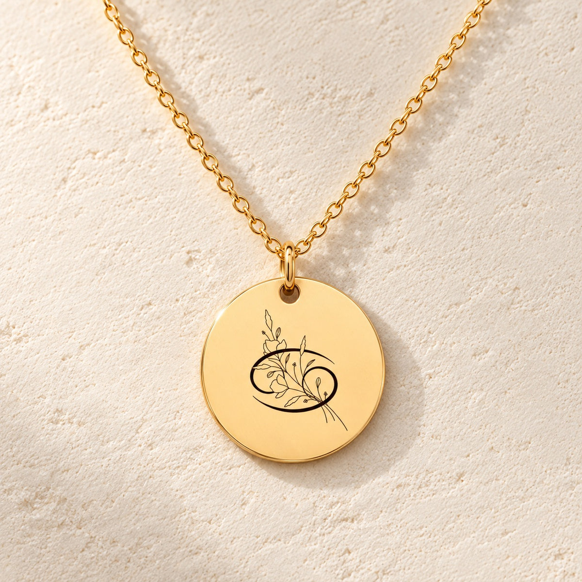 Détail de la médaille ronde dorée avec symbole du signe cancer et fleurs.