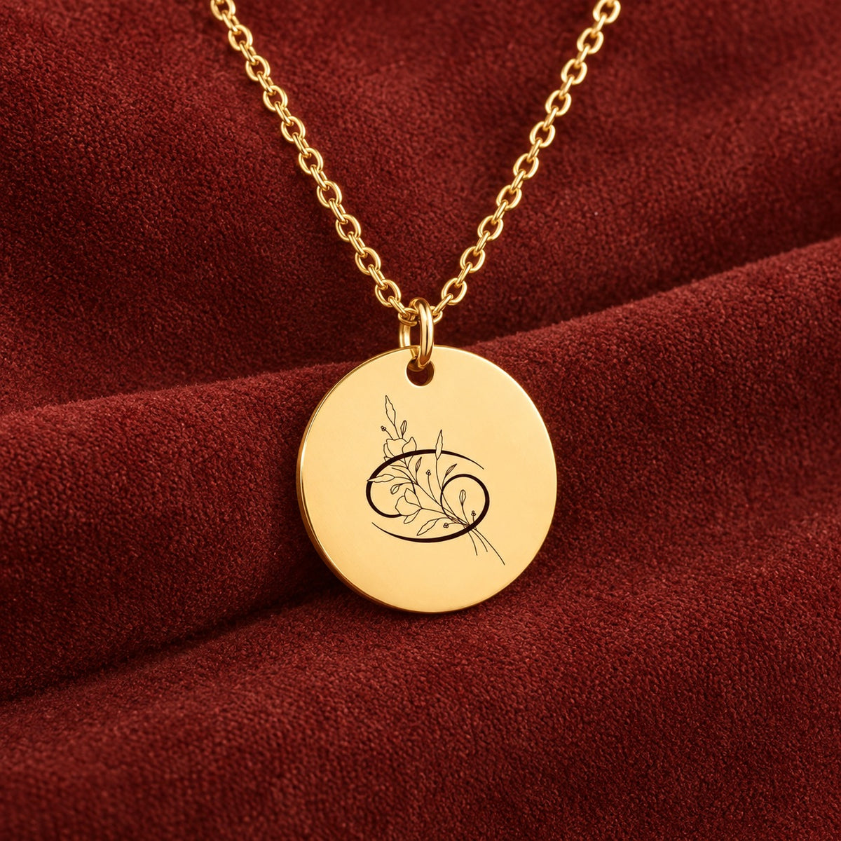Médaille ronde dorée avec symbole du signe cancer et fleurs, sur suédine rouge sanguine.