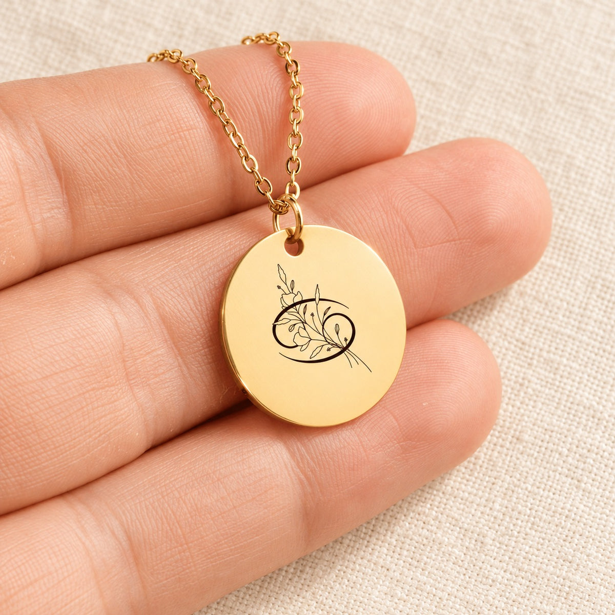 Collier Médaille Florale Signe Astrologique Cancer doré tenu en main, détail de la gravure.