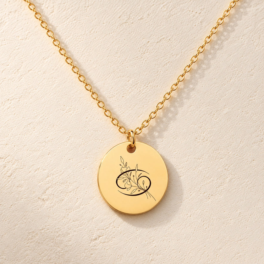 Collier Médaille Florale Signe Astrologique Cancer doré, médaille ronde gravée avec symbole du signe cancer et fleurs, sur fond ivoire.