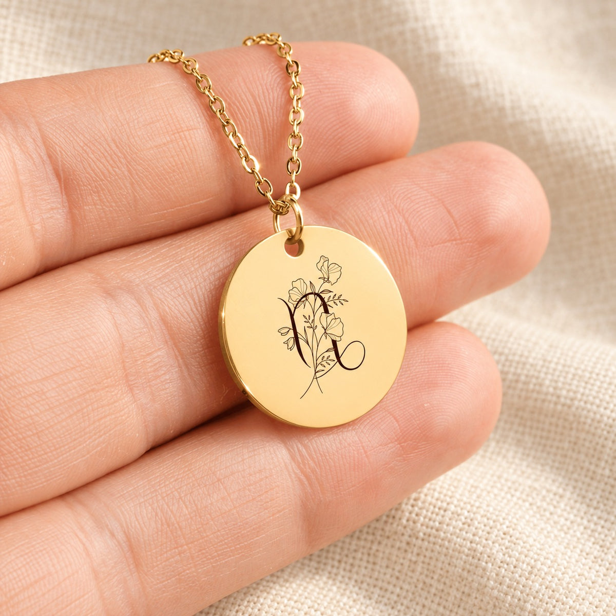 Collier médaille florale signe astrologique Capricorne doré tenu en main, détail de la gravure.