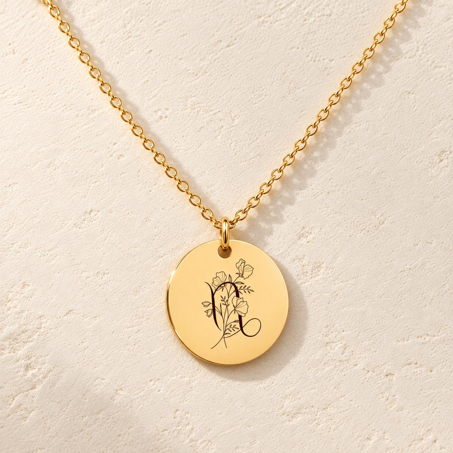 Collier médaille florale signe astrologique Capricorne doré, médaille ronde gravée avec symbole du signe Capricorne et fleurs, sur fond ivoire.