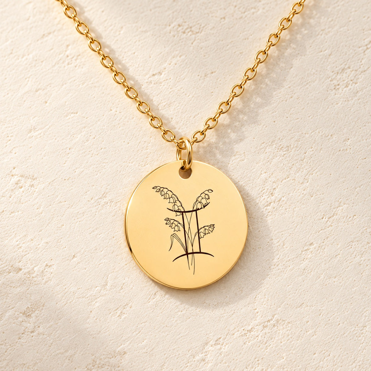 Détail de la médaille ronde dorée avec symbole du signe Gémeaux et fleurs.