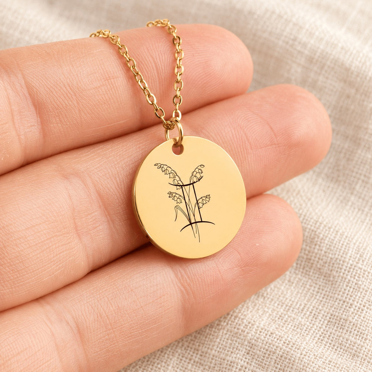 Collier médaille florale signe astrologique Gémeaux doré tenu en main, détail de la gravure.