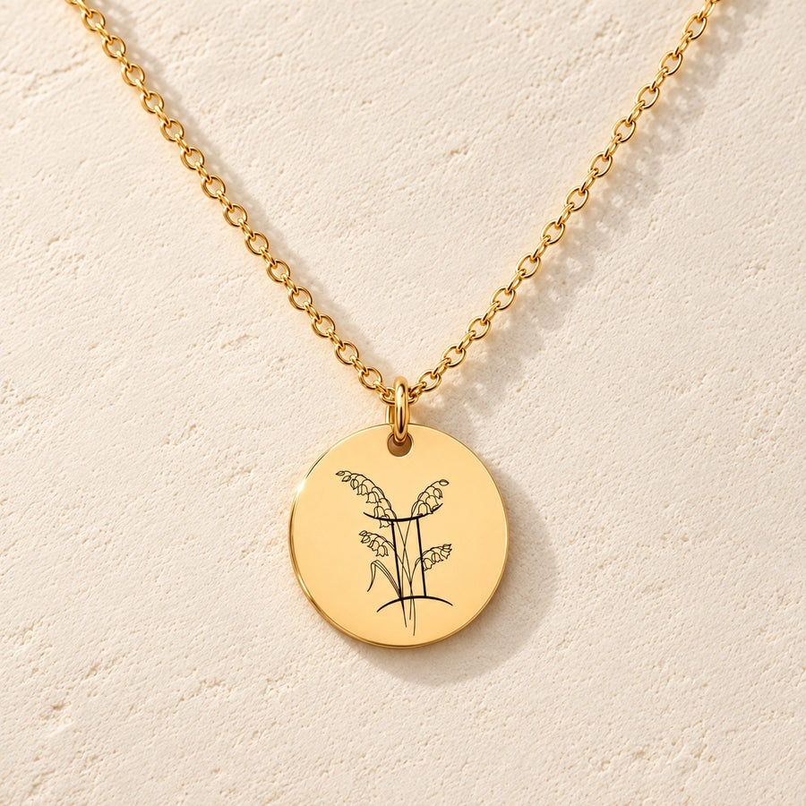 Collier médaille florale signe astrologique Gémeaux doré, médaille ronde gravée avec symbole du signe Gémeaux et fleurs, sur fond ivoire.