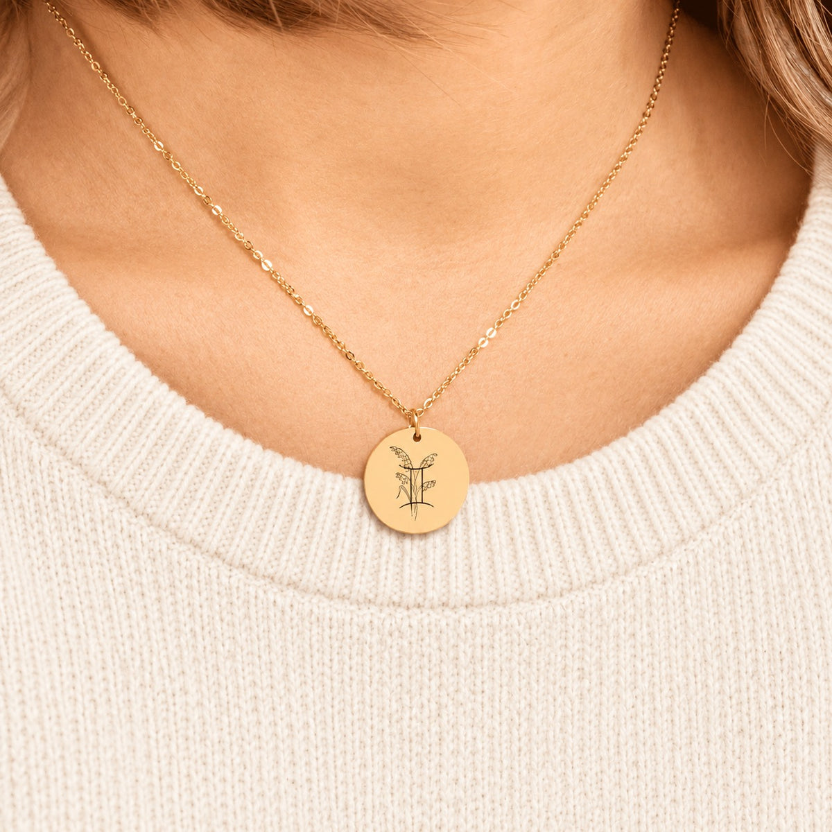 Collier médaille florale signe astrologique Gémeaux doré porté au cou, médaille ronde gravée.