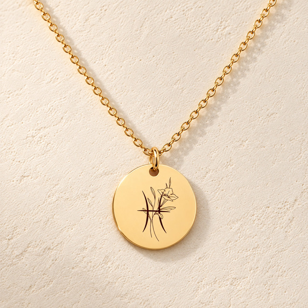 Collier médaille florale signe astrologique Poissons doré, médaille ronde gravée avec symbole du signe Poissons et fleurs, sur fond ivoire.