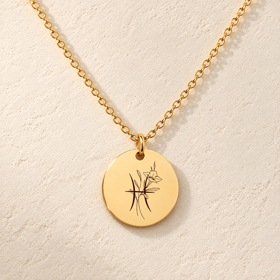 Collier médaille florale signe astrologique Poissons doré, médaille ronde gravée avec symbole du signe Poissons et fleurs, sur fond ivoire.
