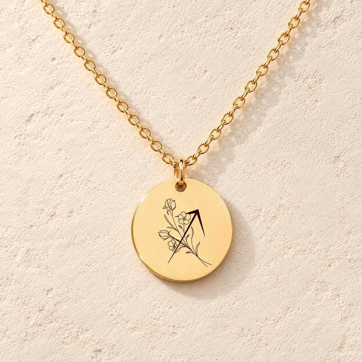 Collier médaille florale signe astrologique Sagittaire doré, médaille ronde gravée avec symbole du signe Sagittaire et fleurs, sur fond ivoire.