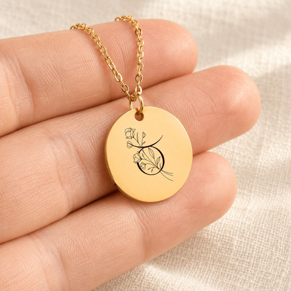 Collier médaille florale signe astrologique Taureau doré tenu en main, détail de la gravure.