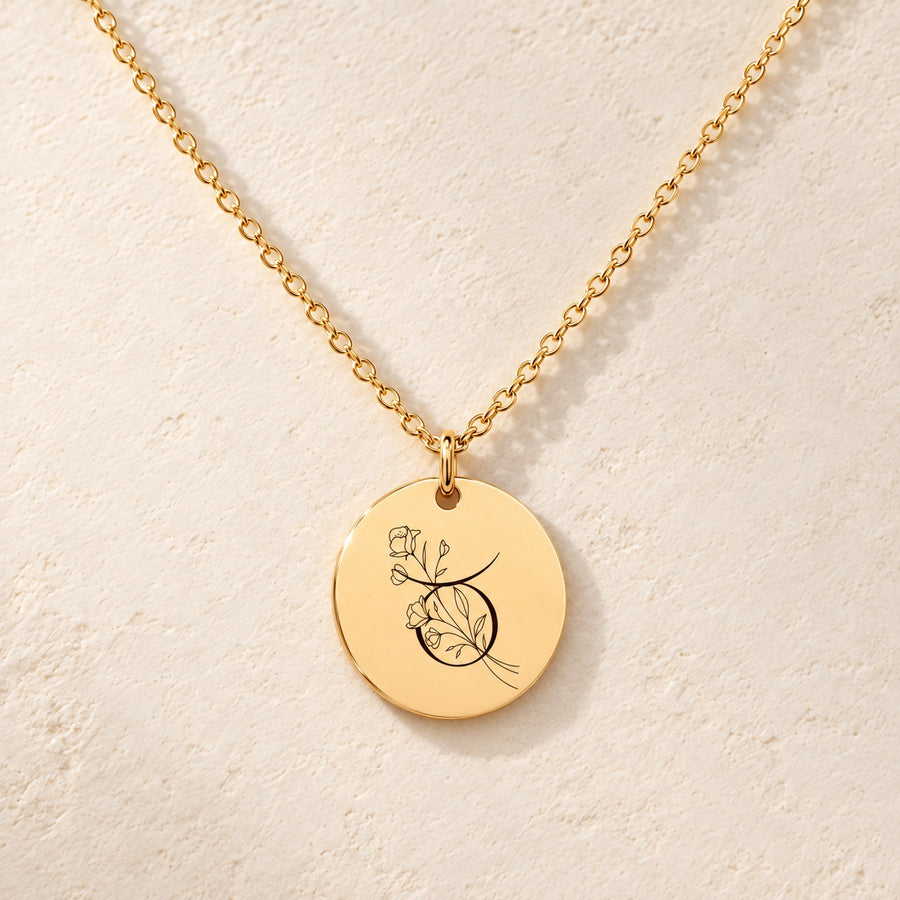 Collier médaille florale signe astrologique Taureau doré, médaille ronde gravée avec symbole du signe Taureau et fleurs, sur fond ivoire.