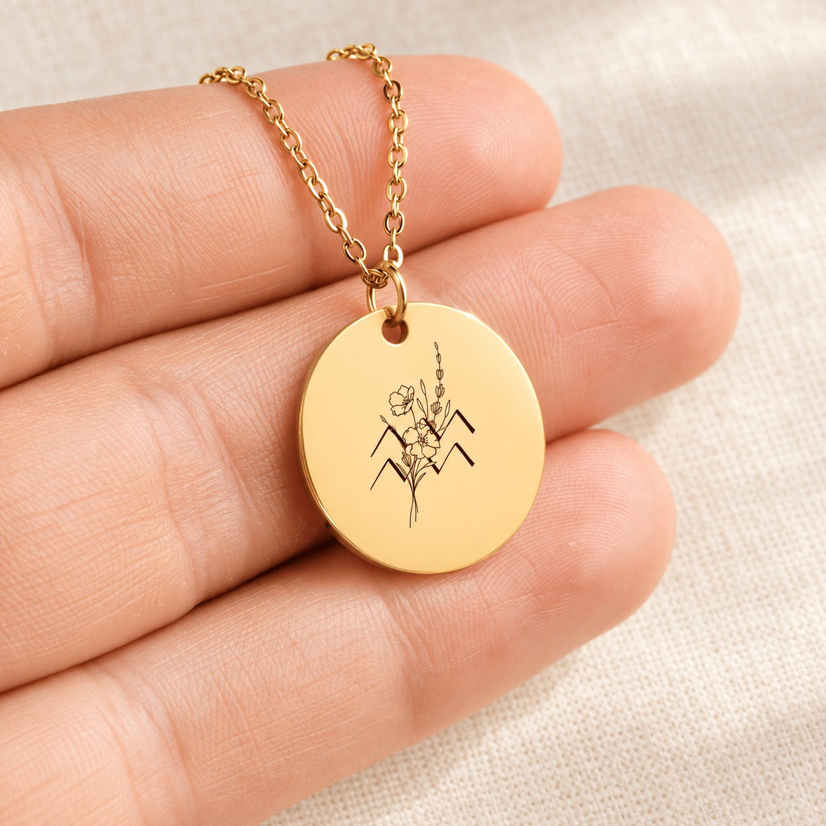 Collier médaille florale signe astrologique Verseau doré tenu en main, détail de la gravure.