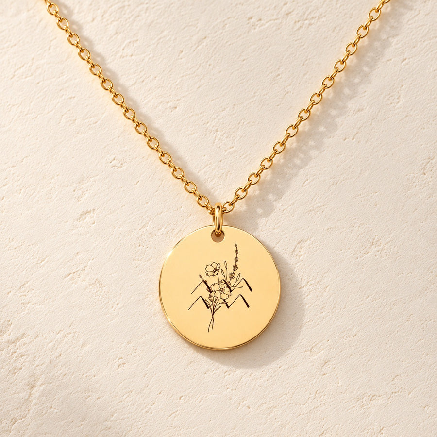Collier médaille florale signe astrologique Verseau doré, médaille ronde gravée avec symbole du signe Verseau et fleurs, sur fond ivoire.