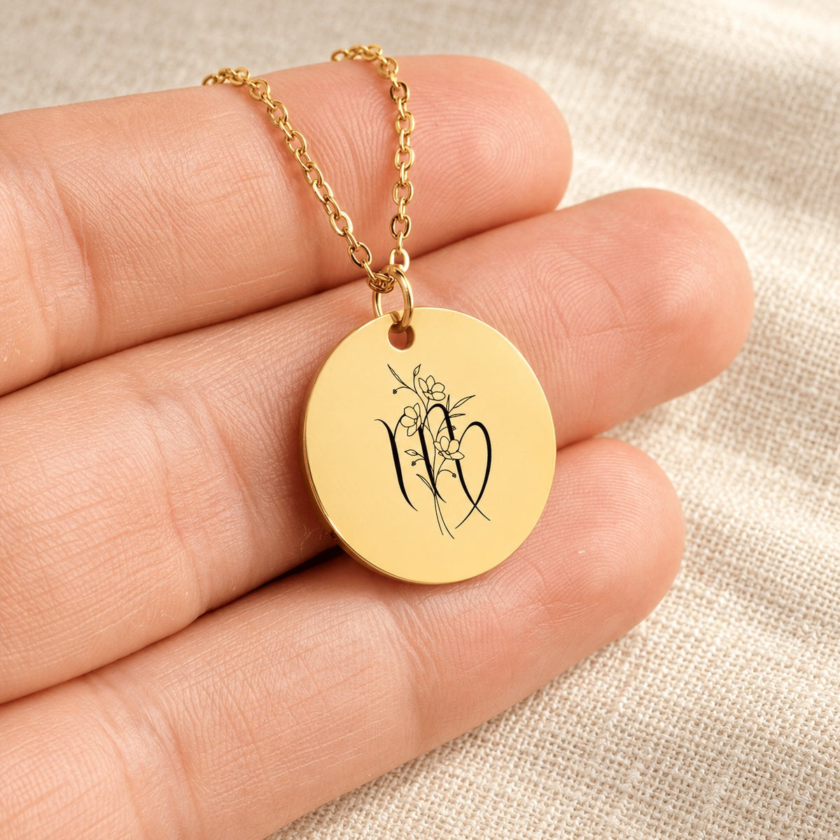 Collier médaille florale signe astrologique Vierge doré tenu en main, détail de la gravure.