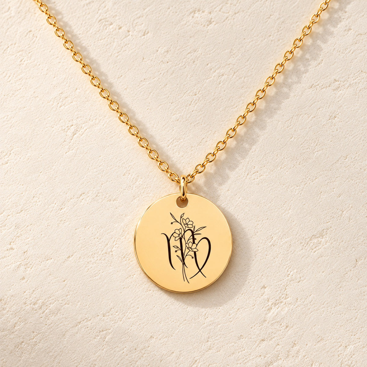 Collier médaille florale signe astrologique Vierge doré, médaille ronde gravée avec symbole du signe Vierge et fleurs, sur fond ivoire.