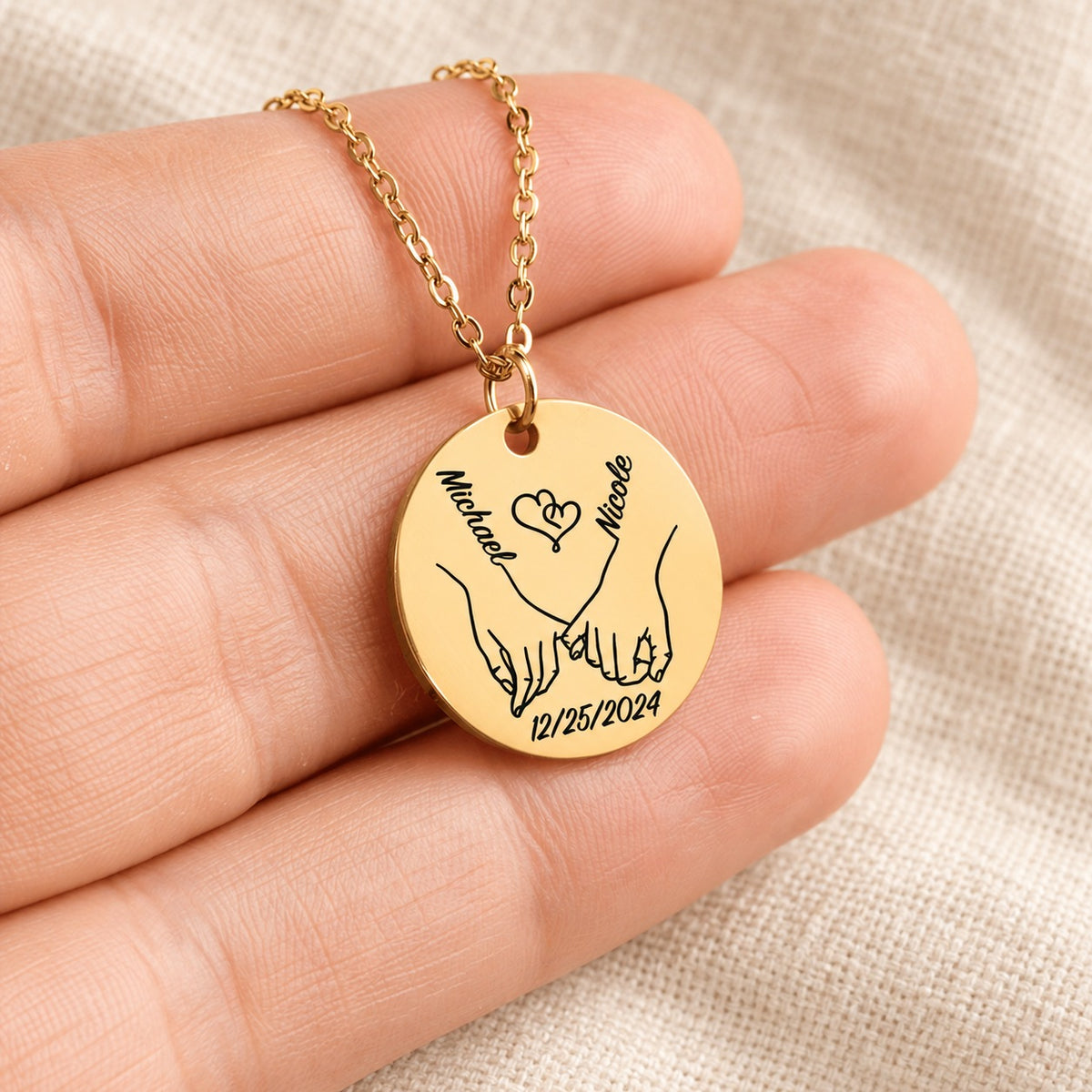 Collier Notre Premier Noël Ensemble personnalisé doré tenu en main, détail de la gravure.