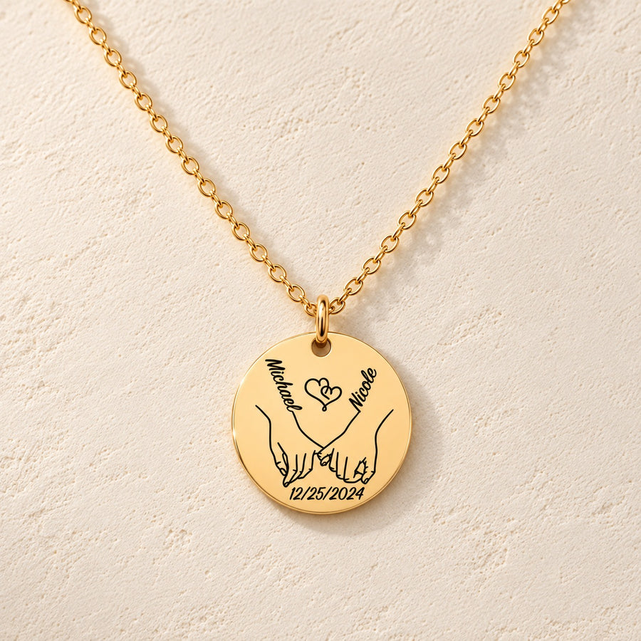 Collier Notre Premier Noël Ensemble personnalisé doré, médaille ronde gravée avec deux mains liées, prénoms Michael et Nicole et date 12/25/2024, sur fond ivoire.