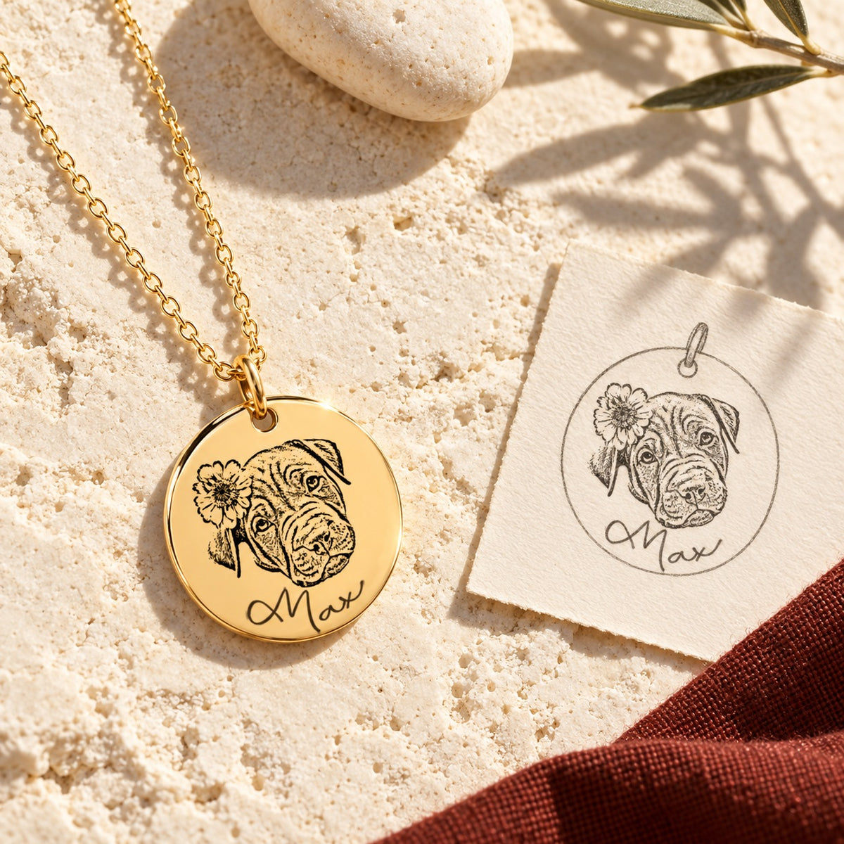Collier portrait de chien Max doré sur pierre claire au soleil, avec dessin du pendentif, ombres d’olivier et étoffe rouge sanguine.