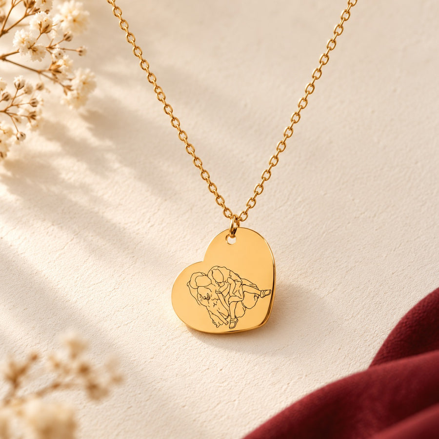 Collier cœur doré avec portrait en line art d’une femme et d’une enfant, sur fond ivoire.