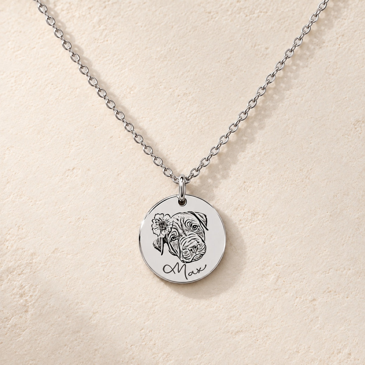 Collier portrait de chien personnalisé argenté, médaille ronde gravée du portrait de Max avec une fleur et de son prénom, sur fond ivoire.