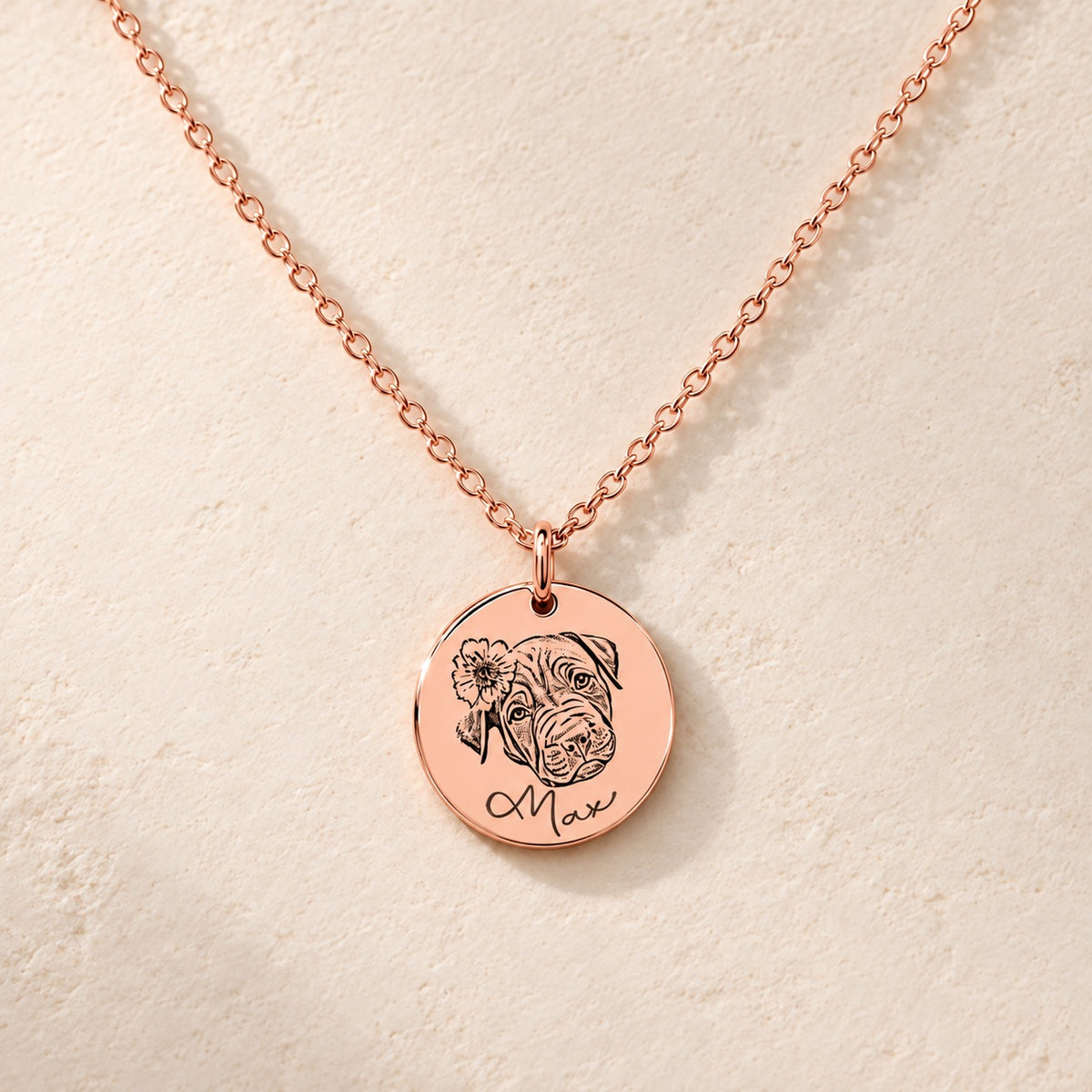 Collier portrait de chien personnalisé en finition or rose, médaille ronde gravée du portrait de Max avec une fleur et de son prénom, sur fond ivoire.
