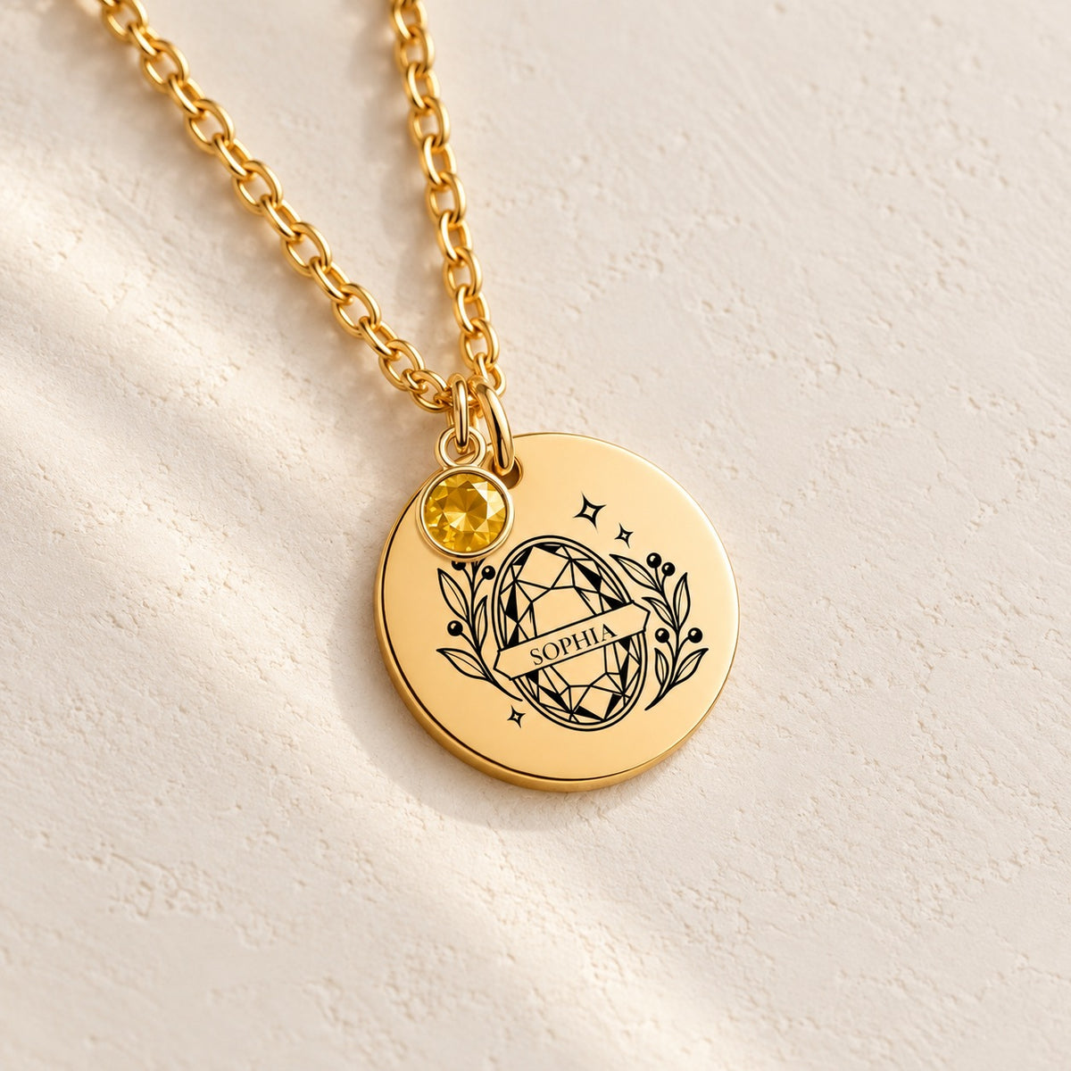 Détail du motif géométrique avec prénom Sophia et pierre jaune gravé sur la médaille ronde dorée, sur fond ivoire.