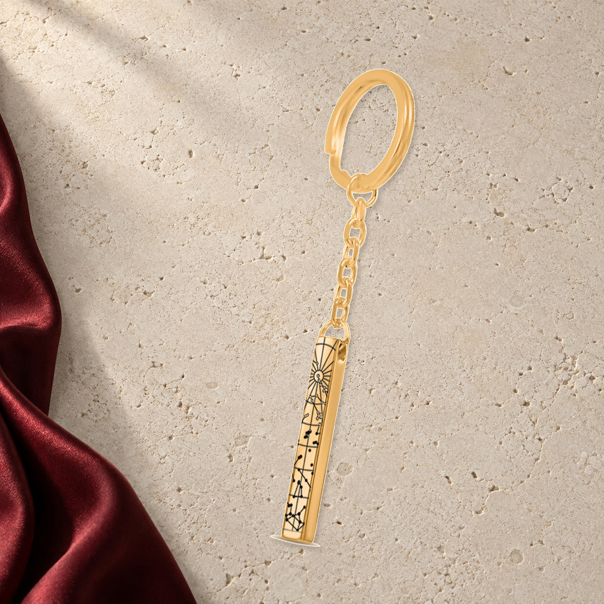 Porte-clés Carte des Étoiles Personnalisé (Barre 3D) en finition dorée sur pierre claire, avec étoffe rouge sanguine ; exemple de personnalisation.
