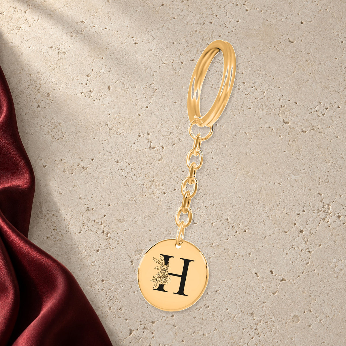 Porte-clés Initiale Florale H Personnalisé en finition dorée sur pierre claire, avec étoffe rouge sanguine ; exemple de personnalisation.