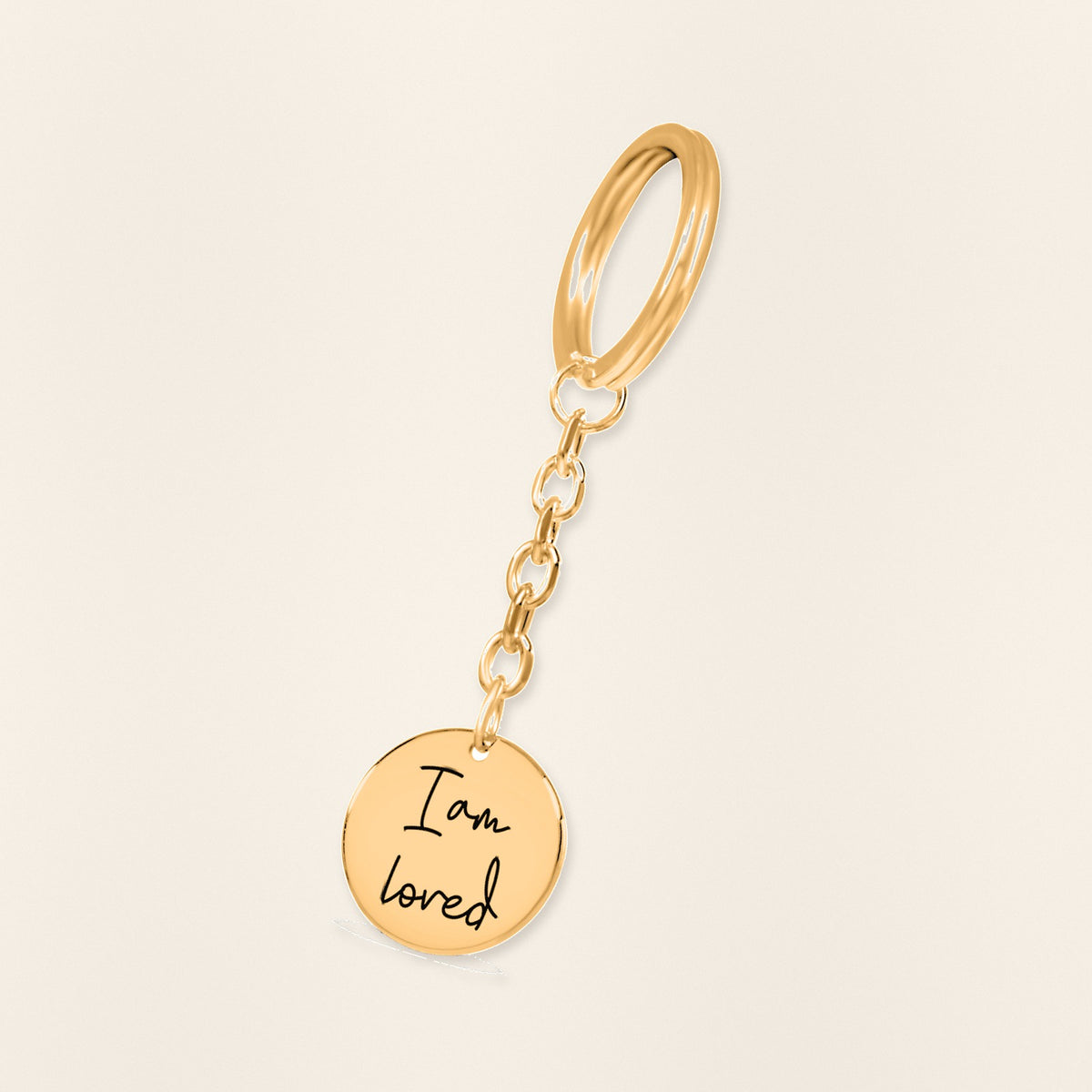 Porte-clés Médaille Affirmations Personnalisée en finition dorée, exemple de gravure sur fond ivoire texturé.