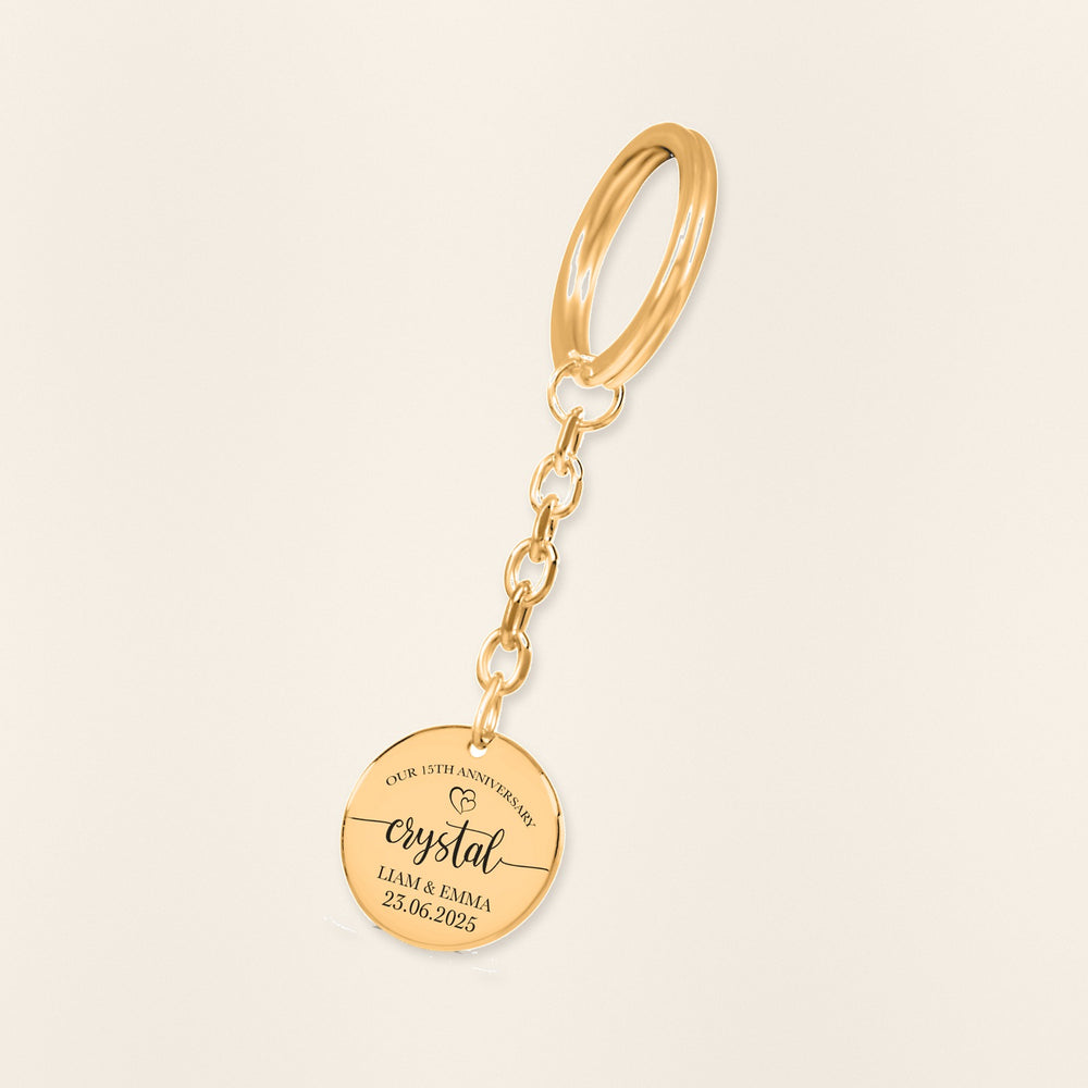 Porte-clés Médaille Anniversaire de Mariage 15 ans (noces de cristal) en finition dorée, exemple de gravure sur fond ivoire texturé.