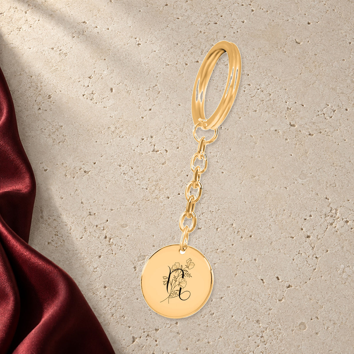 Porte-clés Médaille Florale Signe Astrologique Capricorne en finition dorée sur pierre claire, avec étoffe rouge sanguine ; exemple de personnalisation.