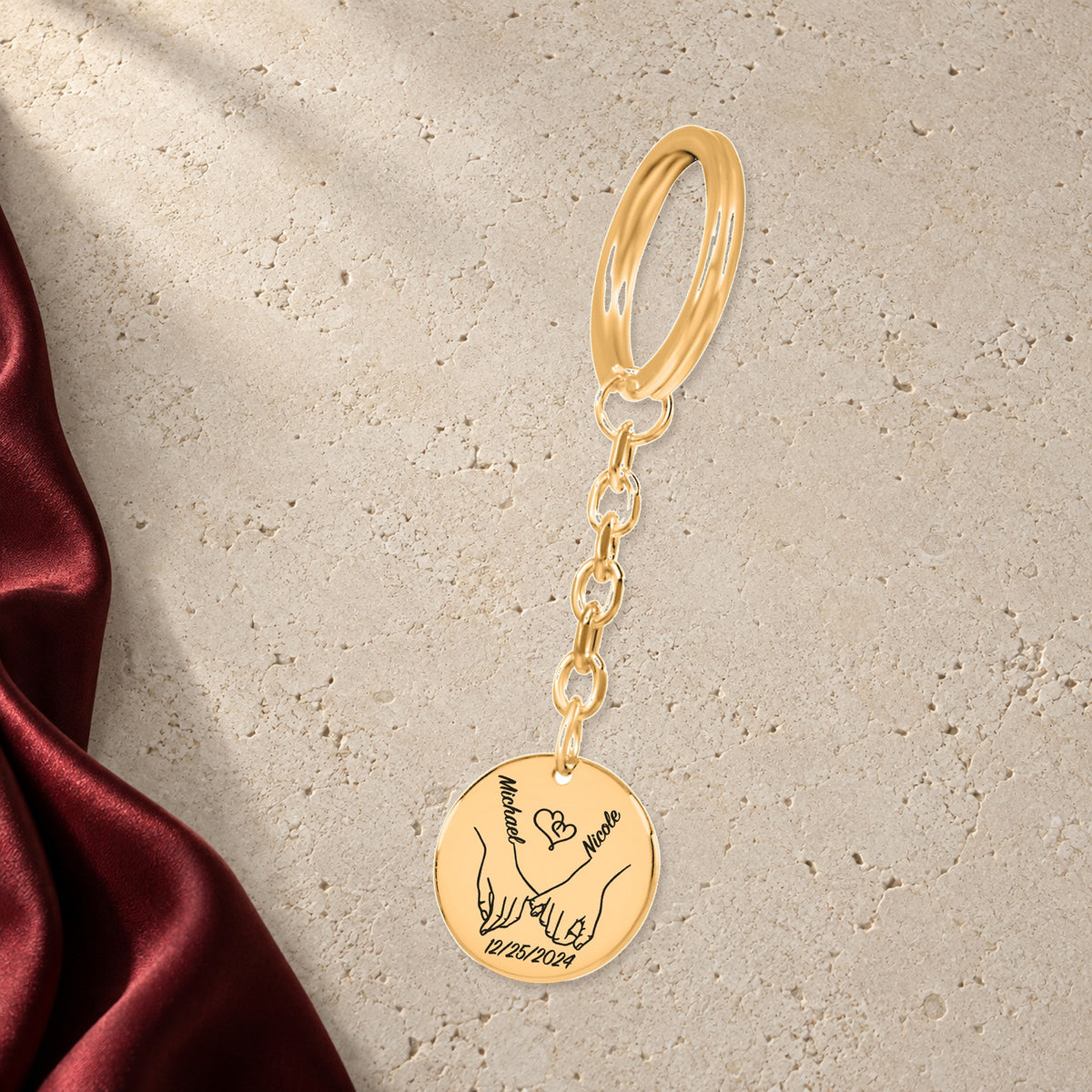 Porte-clés Médaille Notre Premier Noël Ensemble en finition dorée sur pierre claire, avec étoffe rouge sanguine ; exemple de personnalisation.